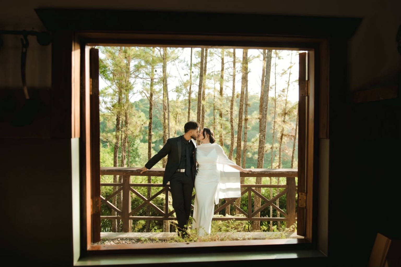 Pareja en un balcón entre árboles, enmarcada por una ventana, fotografía de Enjher Jáquez
